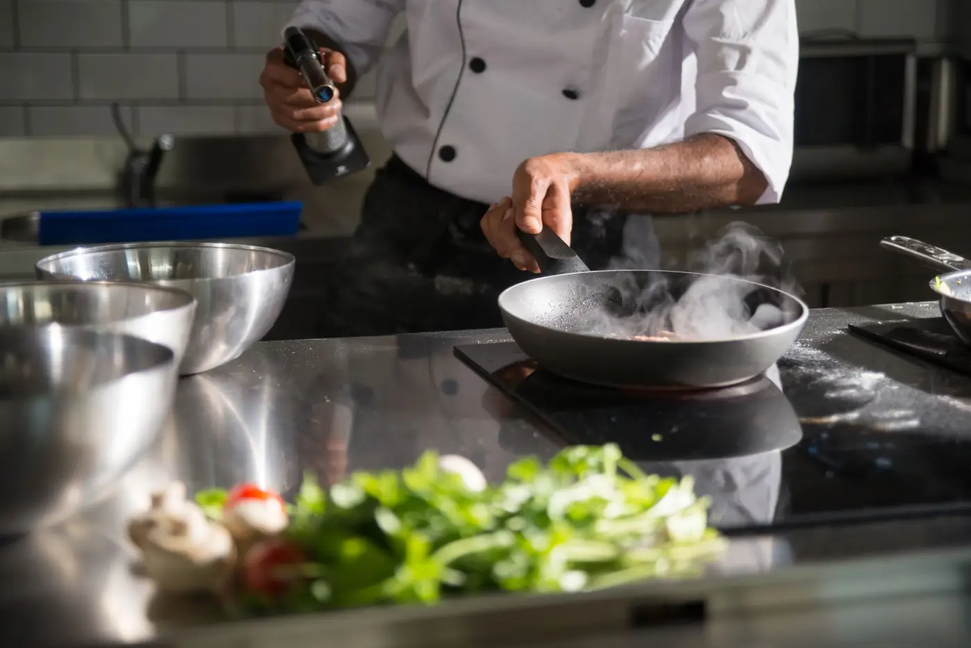 Chef searing in a pan at a steel kitchen counter